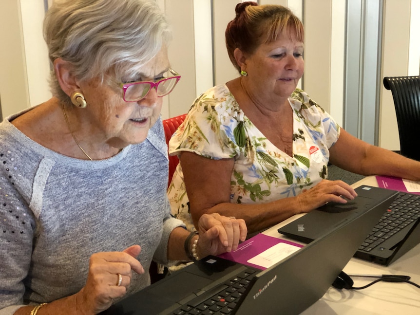 Two older women sitting in front of laptops, focussing on the computer screen.