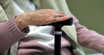 An elderly woman holds a walking stick.