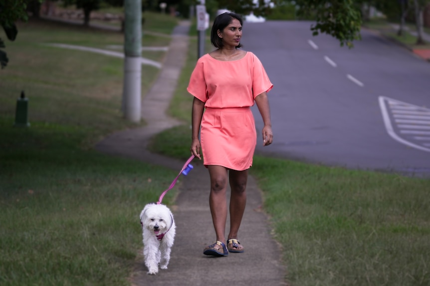 a woman in a pink dress walks a small white dog