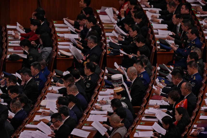 Delegates seated in orderly rows read a work report at the Great Hall of the People in Beijing.