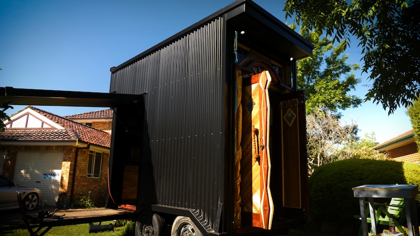 The mobile van is cladded in black corrugated metal and has an ornate timber door.
