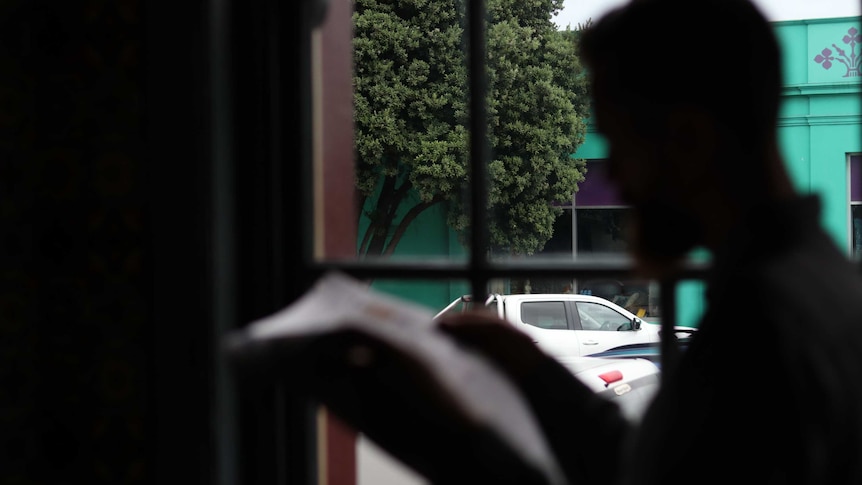 A man in silhouette reading the newspaper in front of a window.