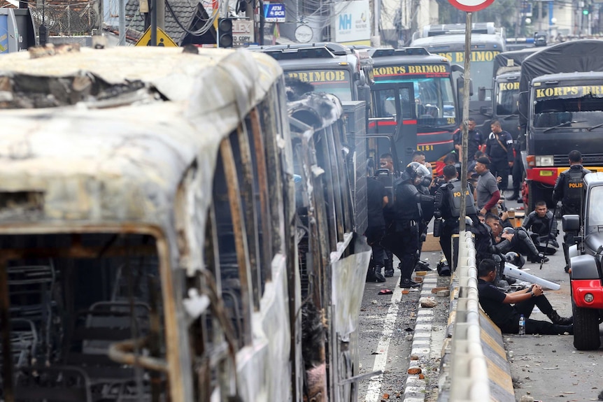 Indonesian police rest near burnt-out buses in Jakarta.