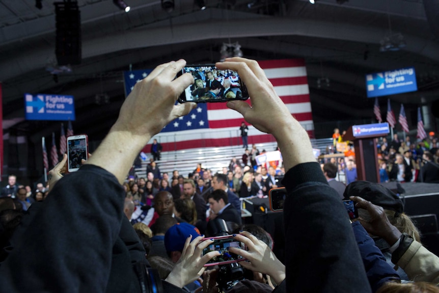 Hands hold a smartphone up over a crowd to film a procession