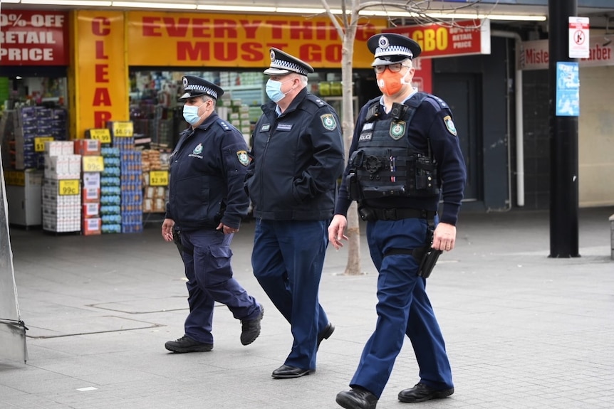 three police officers in masks walking through a shopping strip