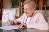 Elderly Launceston woman Joan Webb sitting at her desk, holding a pen.