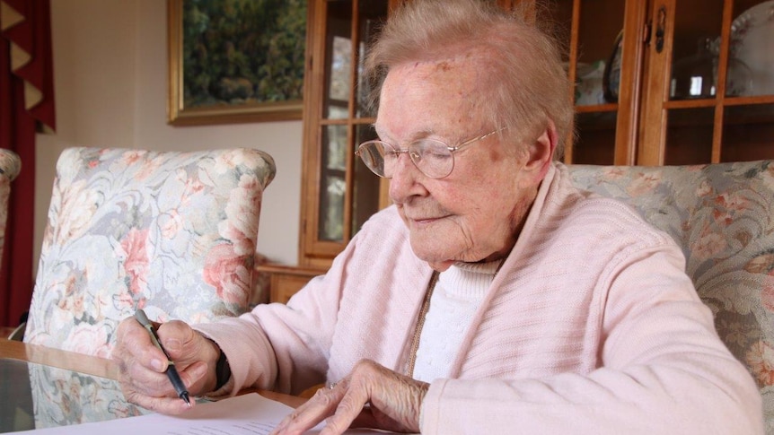 Elderly Launceston woman Joan Webb sitting at her desk, holding a pen.