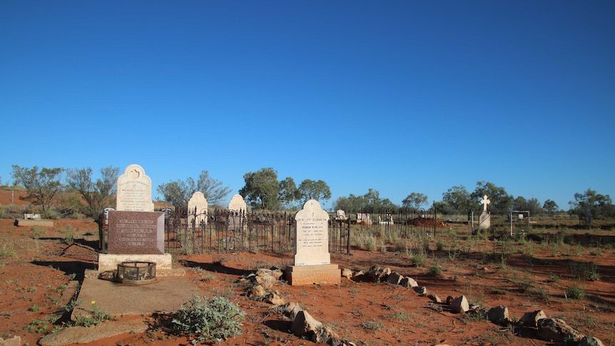 Old tombstones stand among red sand with a big, blue sky