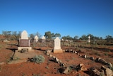 Old tombstones stand among red sand with a big, blue sky