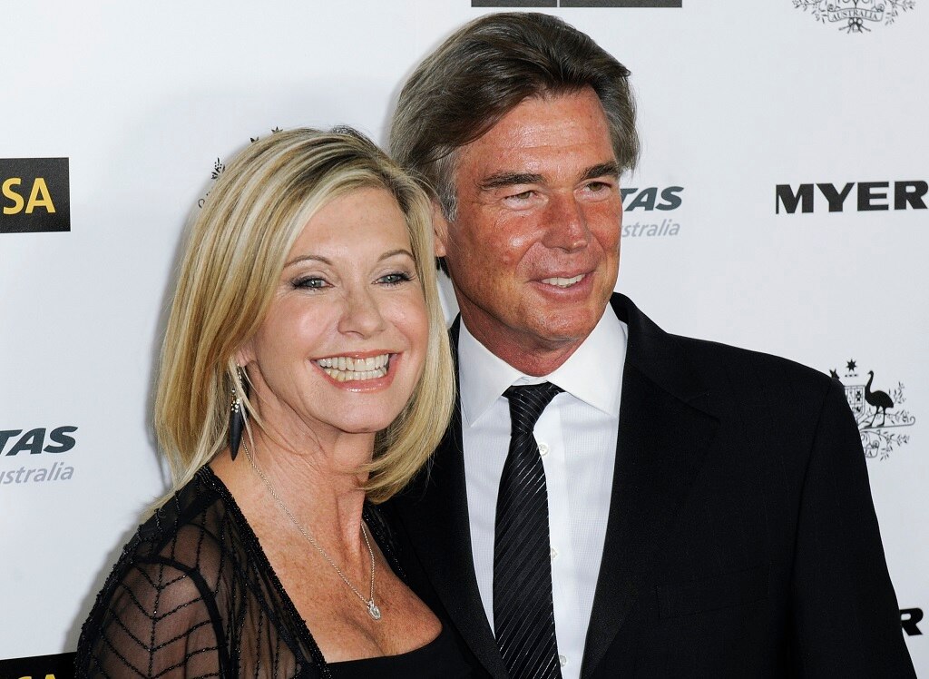 A man and a woman in formal wear smile as they stand together and pose outside an event.