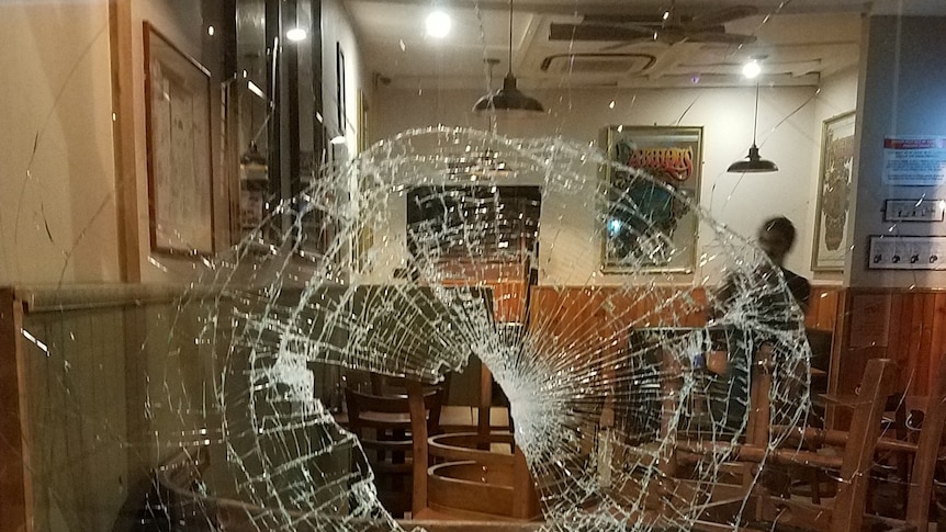 A large hole and smashed in glass in the window of a restaurant