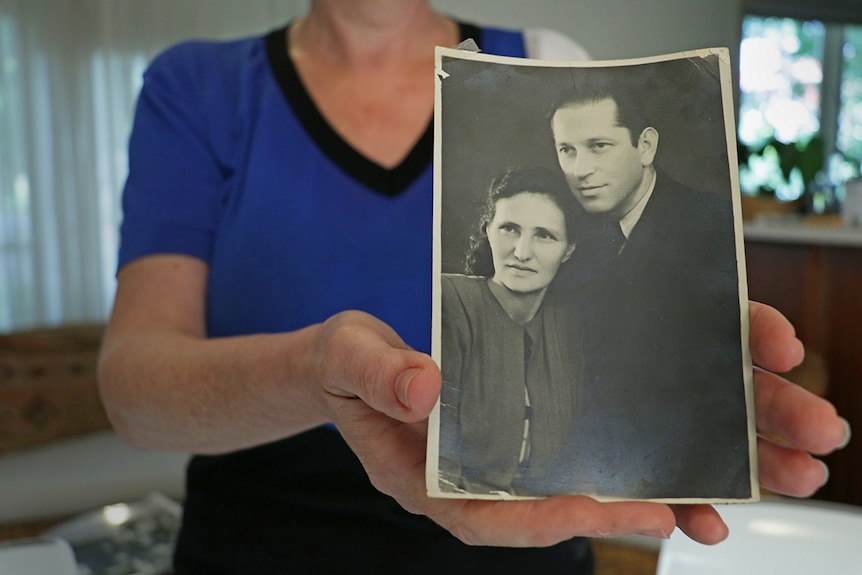Hands hold a black and white photograph of a man and a woman.