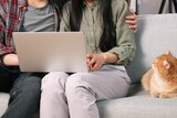 two people sitting on a couch with laptop and cat