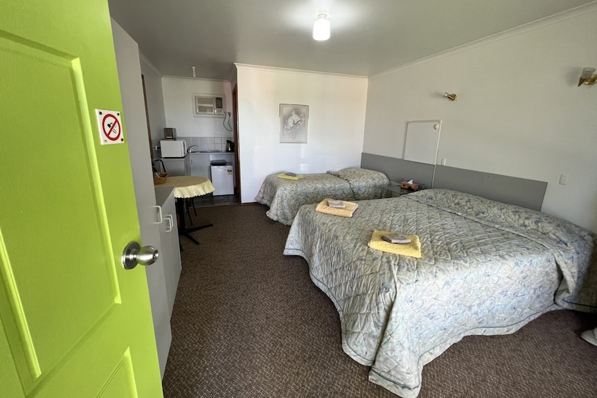 An open lime green door with two double beds beyond it, with folded towels sitting atop