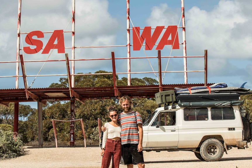 Man and woman standing in front of border crossing sign at South Australian and Western Australian border.