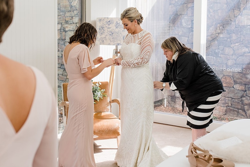 Two women help a bride with her dress