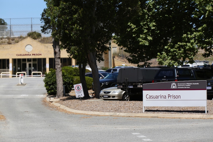A wide shot of the front entrance an to Casuarina Prison with a sign and car park on the right.