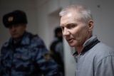 Left is a Russian police officer wearing blue camouflage. Right is an older man with grey hair and a jumper, he looks concerned.
