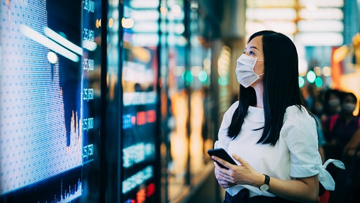 Woman wearing a mask looks at a board showing various data
