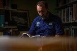 a man wearing a blue shirt reads a book in a dark library
