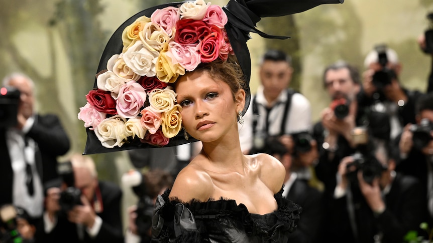A close up of Zendaya wearing a black corset with a headpiece that looks like a bouquet of roses