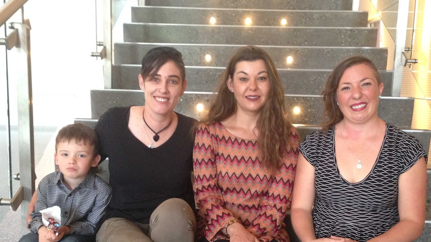 Three women and a small boy sit on stairs and smile at the camera.