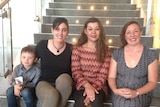 Three women and a small boy sit on stairs and smile at the camera.
