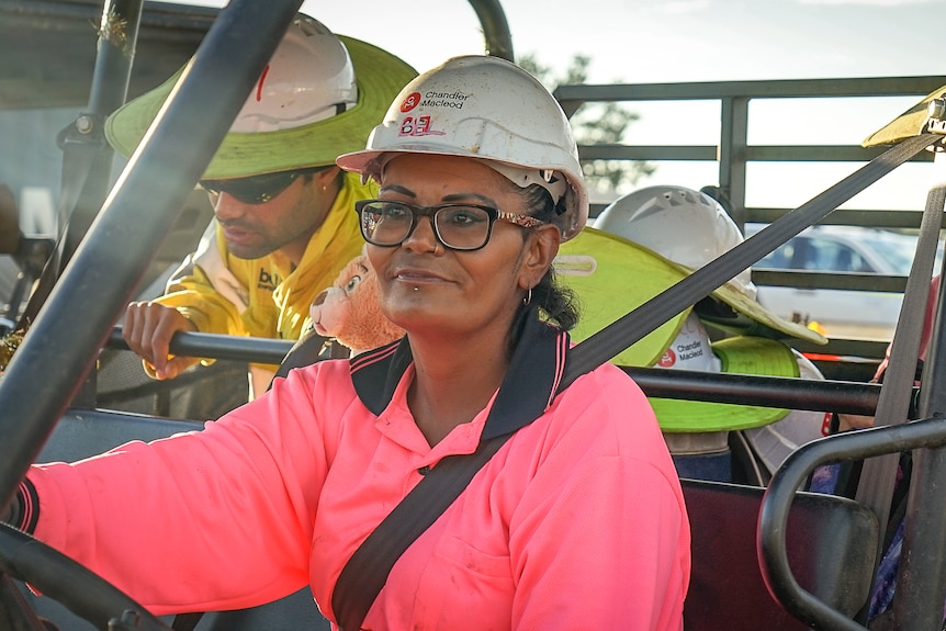 Woman in a hi-vis pink work uniform and hard hat sitting in a vehicle.