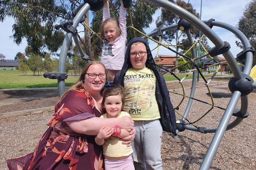 A woman with three small children in a park in front of play equipment.