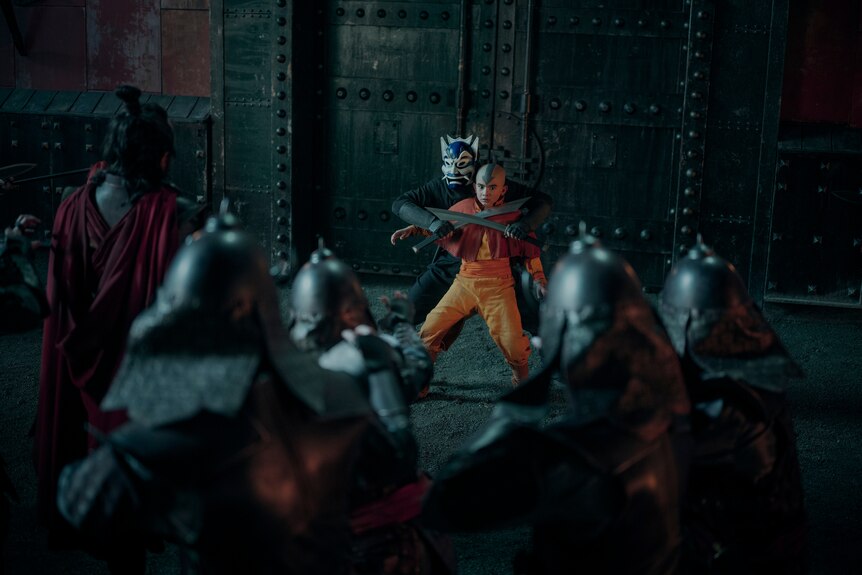 A TV still of Gordon Cormier, a Canadian Filipino teenager dressed as Avatar. Someone in a mask holds swords to his throat.