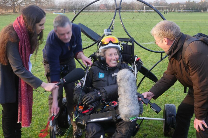 A woman in paramotor surrounded by reporters.