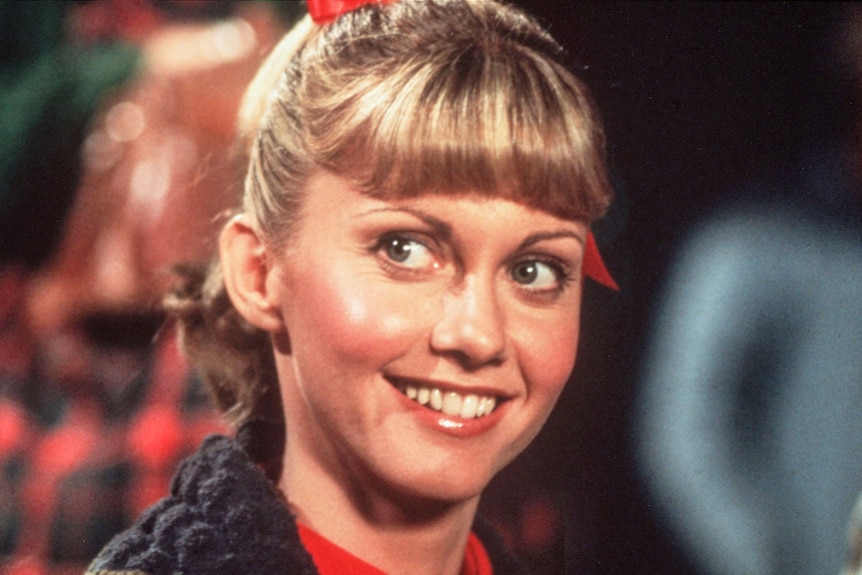 Closeup of a young Olivia Newton-John as Sandy in Grease. Her bright eyes are looking upwards and she has a blonde fringe