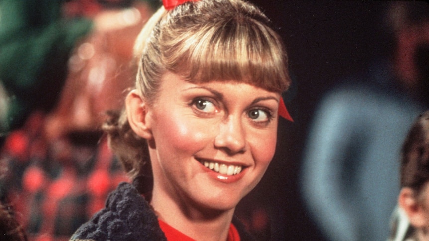 Photo of Olivia Newton-John in the film Grease as the character Sandy. She is smiling at the camera 