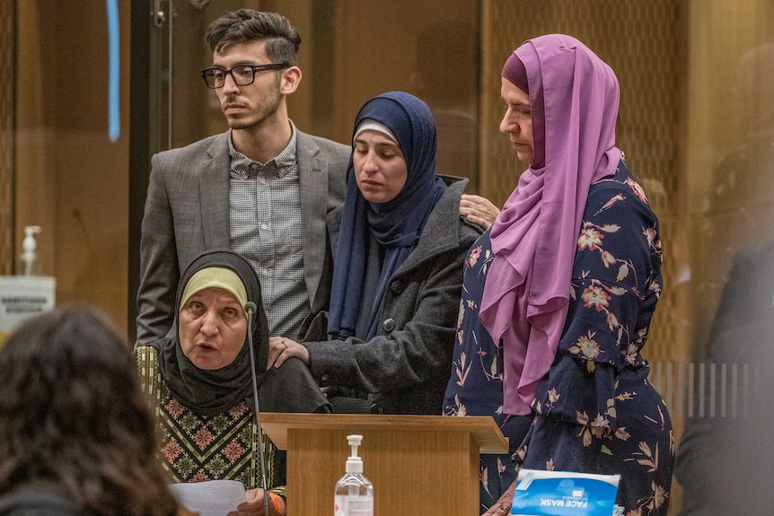 A woman in a hijab sits in a court room speaking, while surrounded by a young man and two women in hijabs