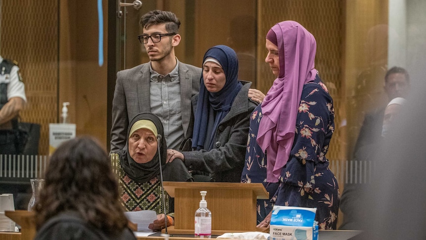 A woman in a hijab sits in a court room speaking, while surrounded by a young man and two women in hijabs