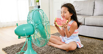 A girl eats a watermelon in front of a fan