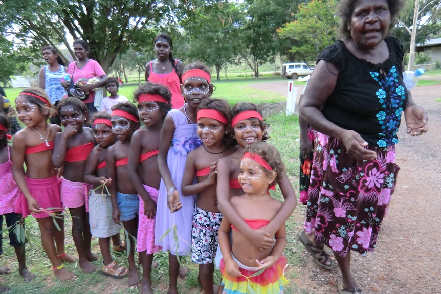 A group of smiling children line up painted in traditional Aboriginal style