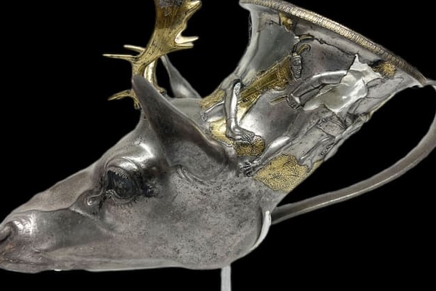 A metal vessel in the form of a stag's head, with gold highlights.