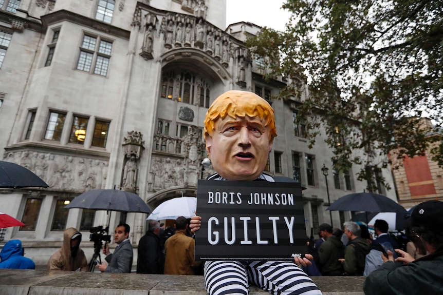 A man dressed up as Boris Johnson stands outside the Supreme Court. He wears a black and white stripe prison outfit.