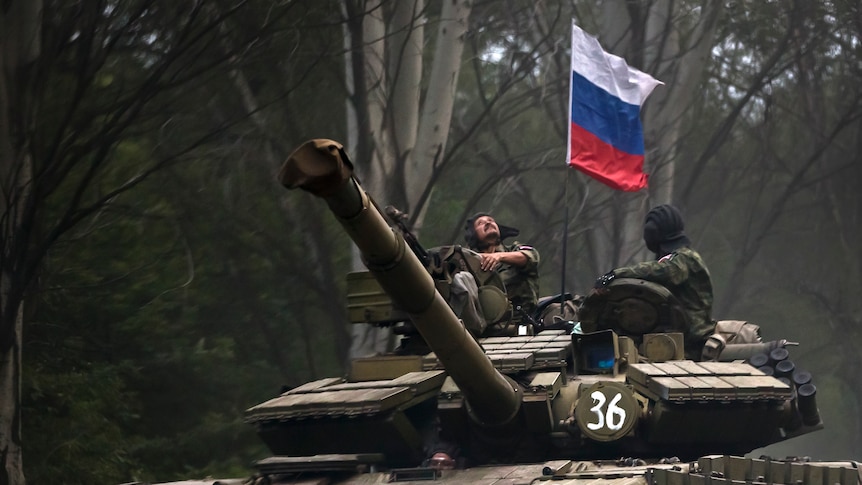 A pro-Russian rebel looks up while riding on a tank flying Russia's flag