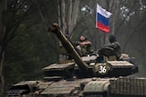 A pro-Russian rebel looks up while riding on a tank flying Russia's flag