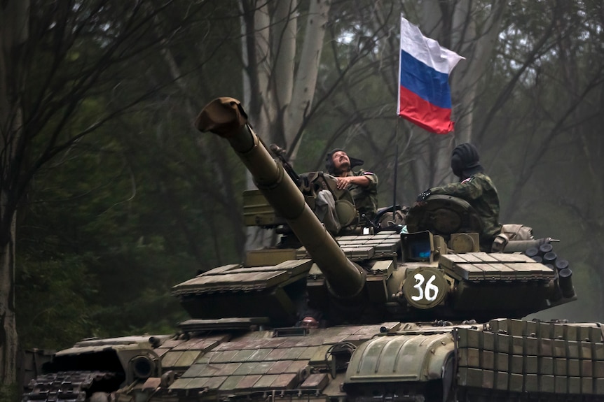 A pro-Russian rebel looks up while riding on a tank flying Russia's flag