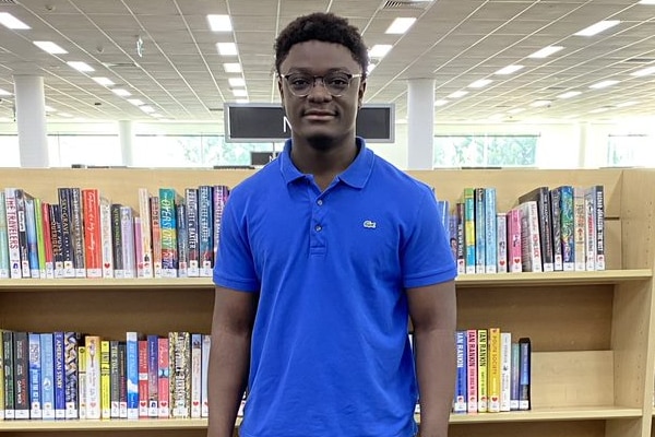 A young African-Australian wearing blue shirt posing in front of book shelves in library 