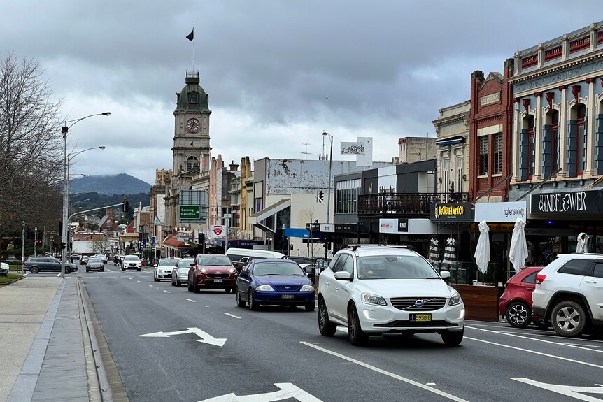 Cars drive down a main road, with buildings and mountains in the background.