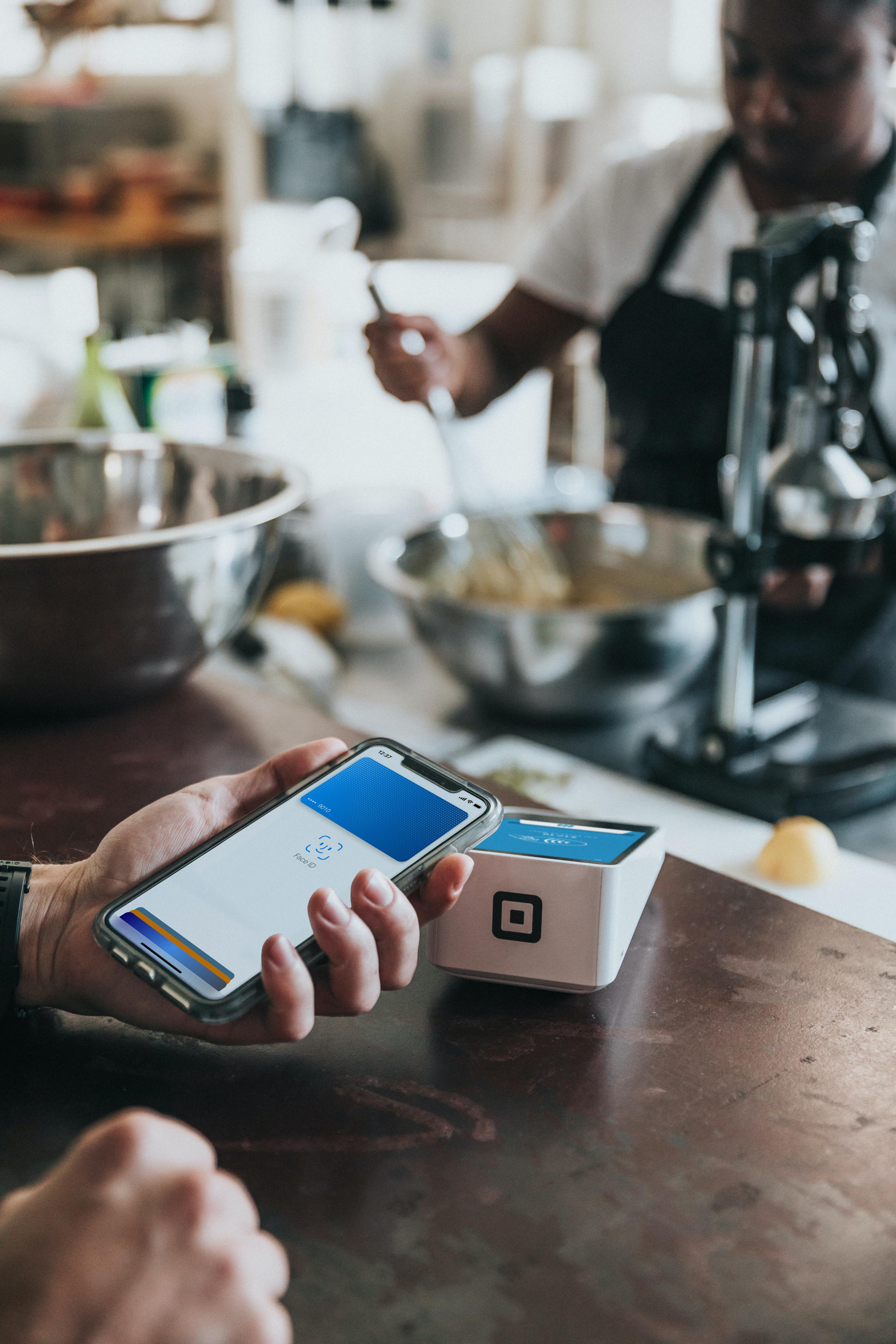 A hand places their smart phone near a sleek Eftpos machine on the wooden counter of a cafe.