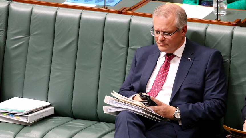 Scott Morrison looks at his phone in Parliament