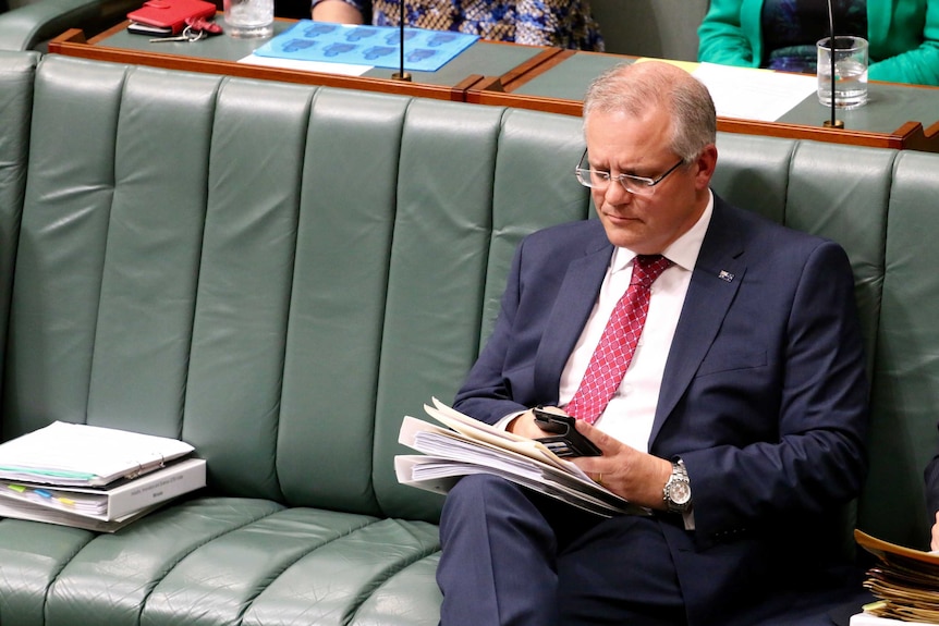 Scott Morrison looks at his phone in Parliament