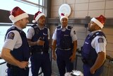Four men in police uniforms and Santa hats stand in a stairwell singing.