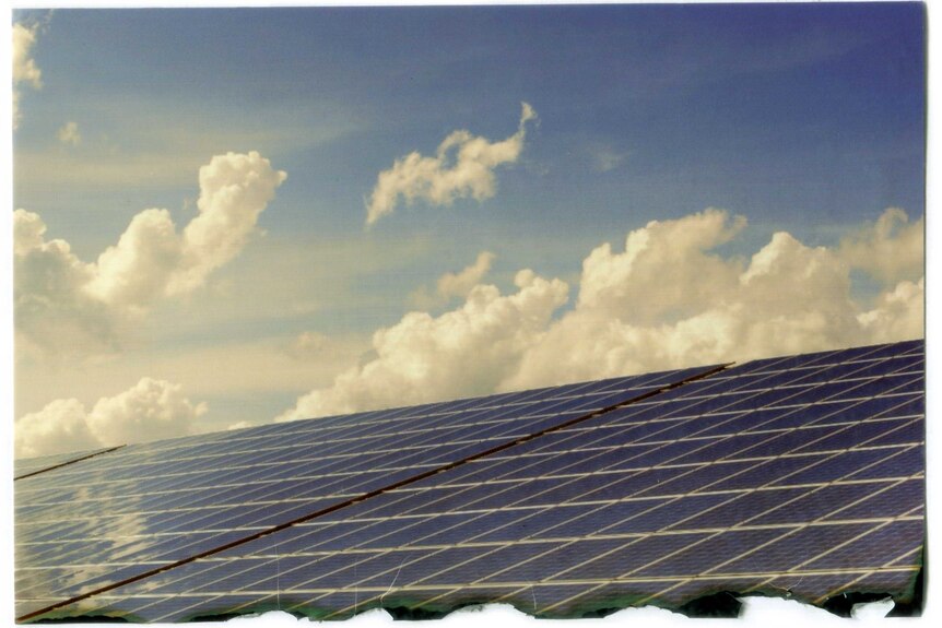 Solar panels in front of a cloud-filled blue sky.