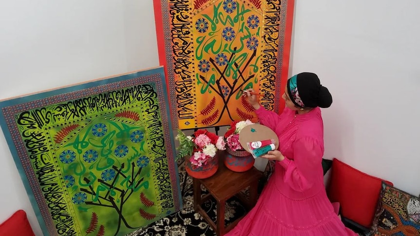 A woman facing a canvas painting. On the canvas is Arabic script